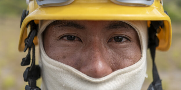 Indigener Mann mit gelbem Schutzhelm und Mundschutz